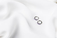 A pair of silver earrings with purple cubic zirconias on a white cloth background