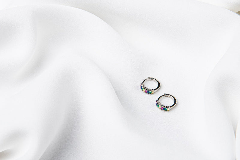 A pair of silver earrings with rainbow cubic zirconias on a white cloth background