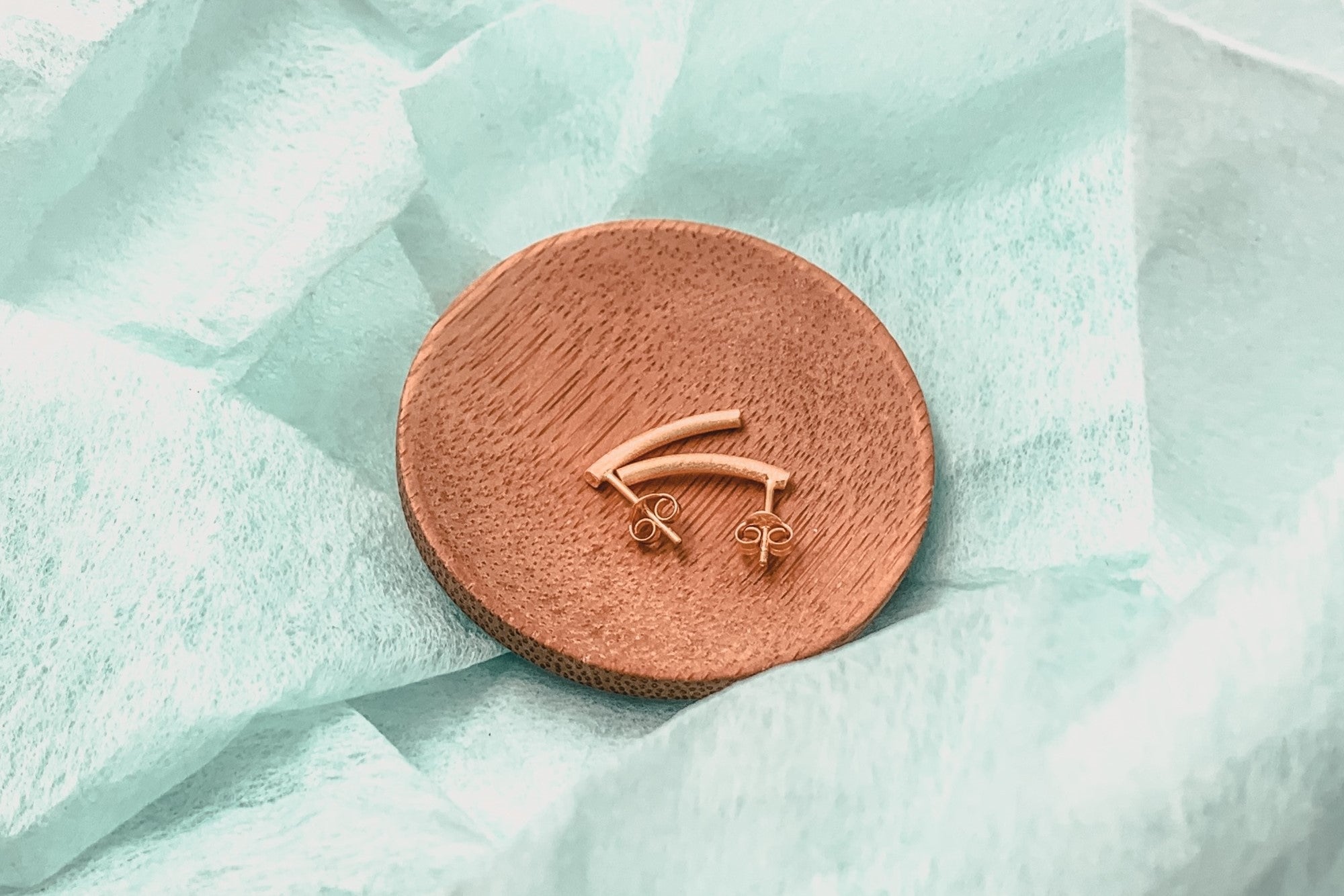 A pair of rose gold stud earrings with butterfly backs, displayed on a wood surface.
