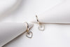 A pair of silver hoop earrings with heart-shaped dangles, displayed on a white background.