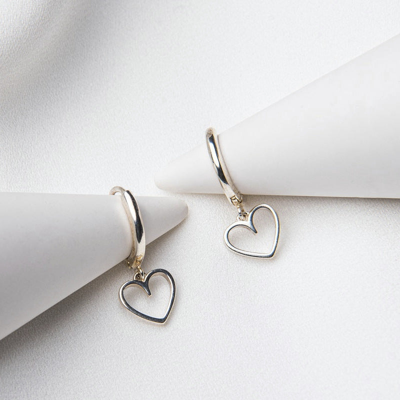 A pair of silver hoop earrings with heart-shaped dangles, displayed on a white background.