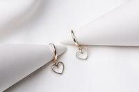 A pair of silver hoop earrings with heart-shaped dangles, displayed on a white background.