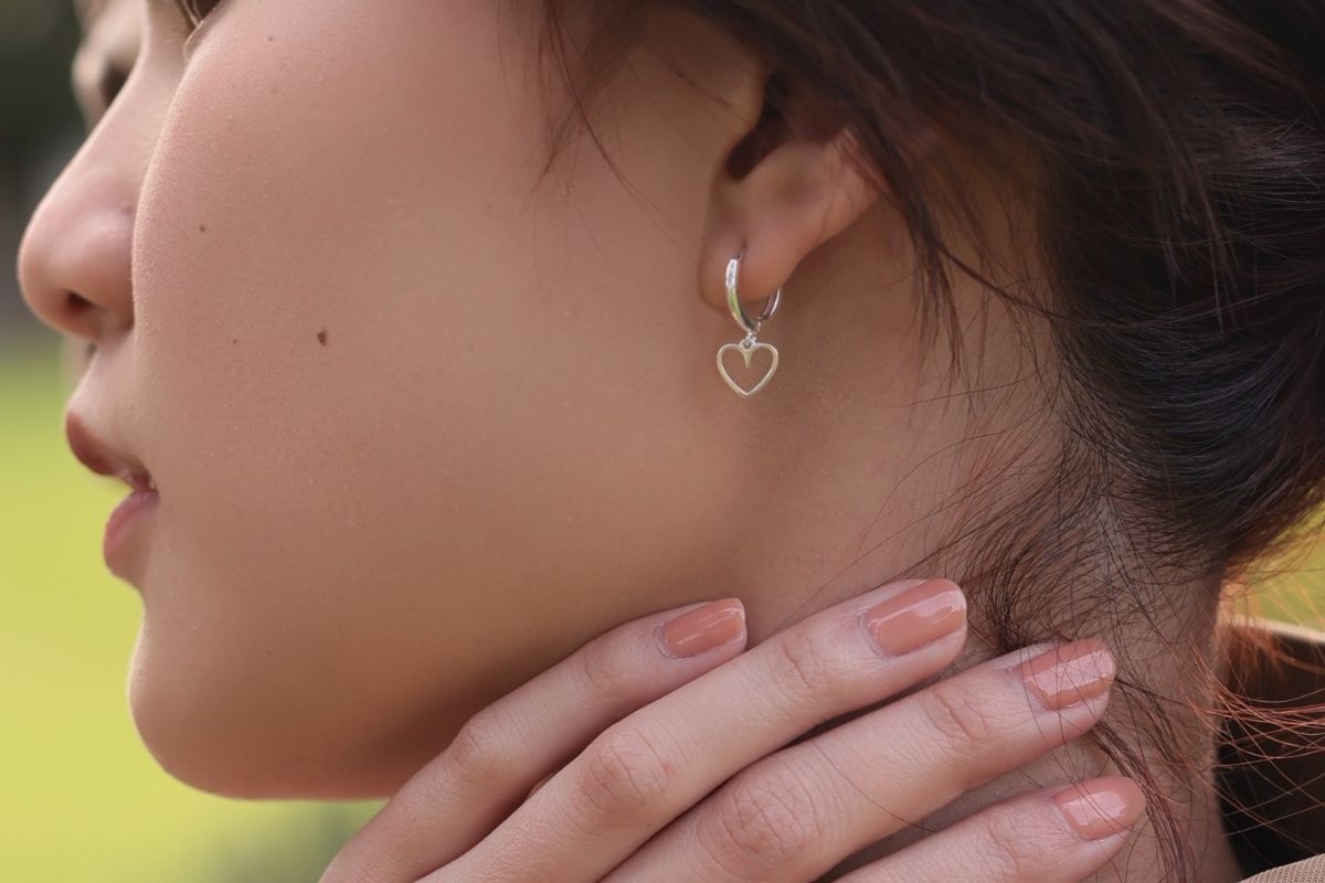 A women wearing a pair of silver hoop earrings with heart-shaped dangles.
