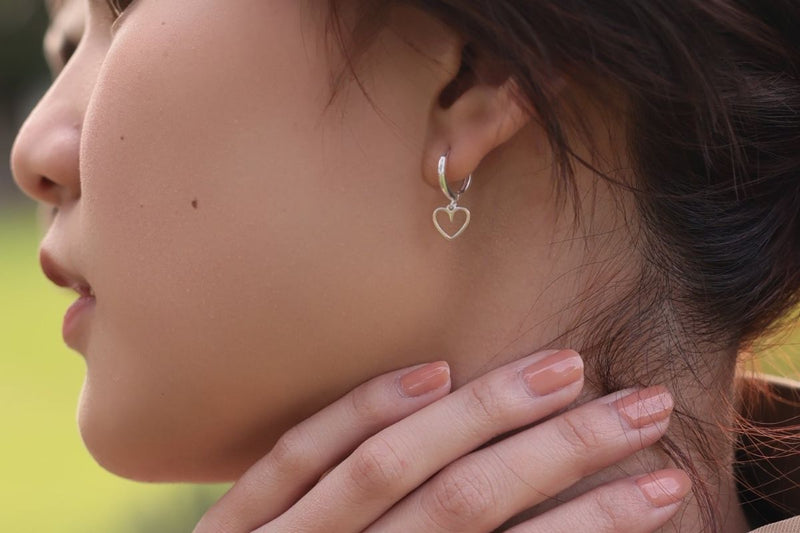 A women wearing a pair of silver hoop earrings with heart-shaped dangles.