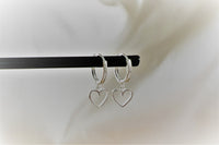 A pair of silver hoop earrings with heart-shaped dangles, displayed on a white background.