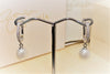 A pair of silver earrlings featureing cubic zirconas and white pearls on a earring display stand with a blurred background