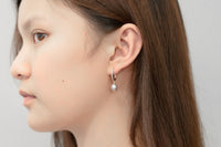 A silver earring with a white pearl worn by a woman