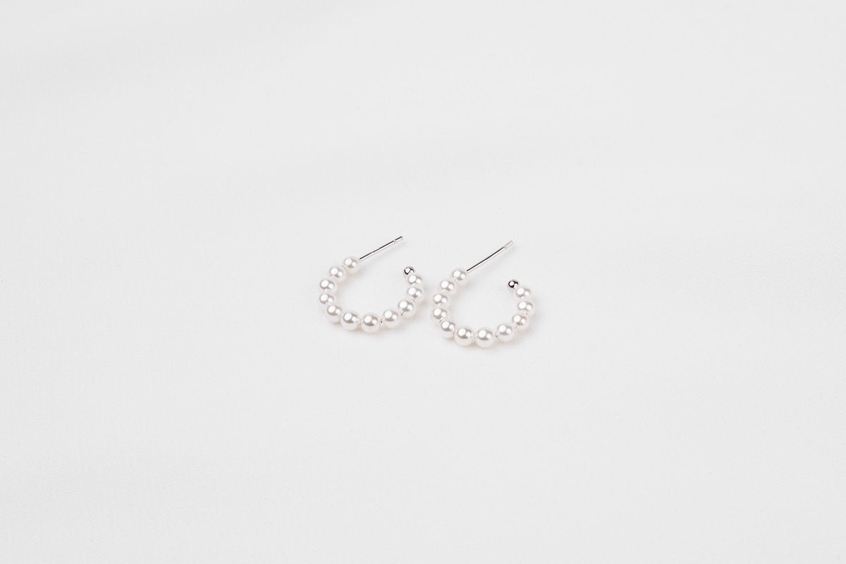 A pair of silver pearl earrings with a semi-dangle design on a white background.