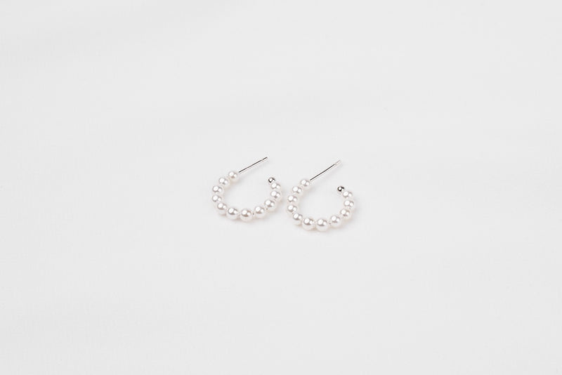 A pair of silver pearl earrings with a semi-dangle design on a white background.