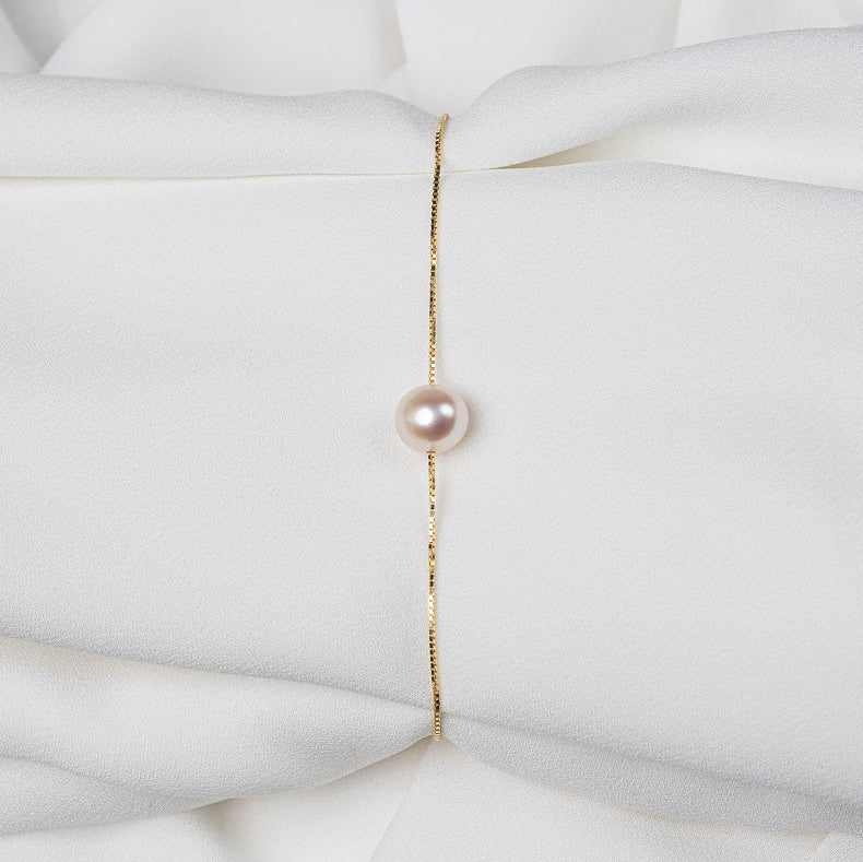 Fine gold chain bracelet featuring a single rose pearl on a white cloth background