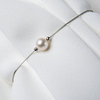 A sterling silver bracelet with a pearl pendant on a white silky fabric surface.