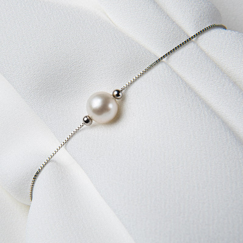 A sterling silver bracelet with a pearl pendant on a white silky fabric surface.