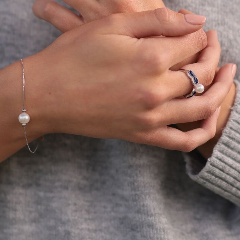 Close up of a woman wearing a fine silver chain bracelet featuring a single white pearl.