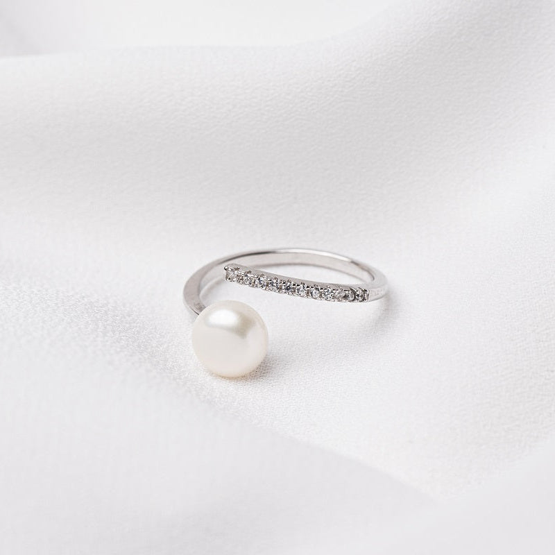 A silver ring featureing a white pearl and cubic zirconias on the band. All on a white background