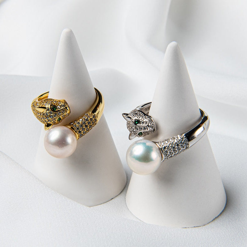 Two rings on white pedestals, one with a gold vermeil finish and a panther design, silver finish and a panther design. Both with a pearl centrepeice.
