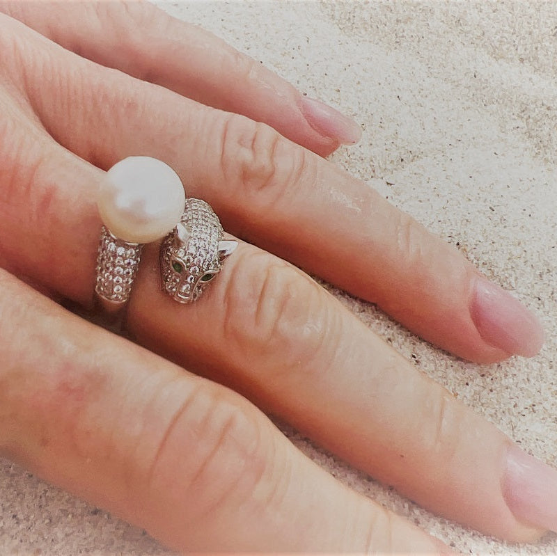A close up of a woans hand wearing a silver panther design ring featuring a white pearl centerpiece.