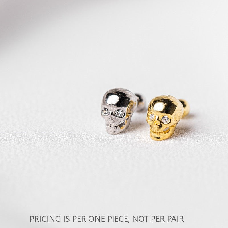A pair of skull-shaped stud earrings with gold vermeil coating over sterling silver 925, displayed on a white textured surface.
