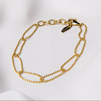 A sterling gold chain bracelet with a clasp, placed on a white fabric surface.