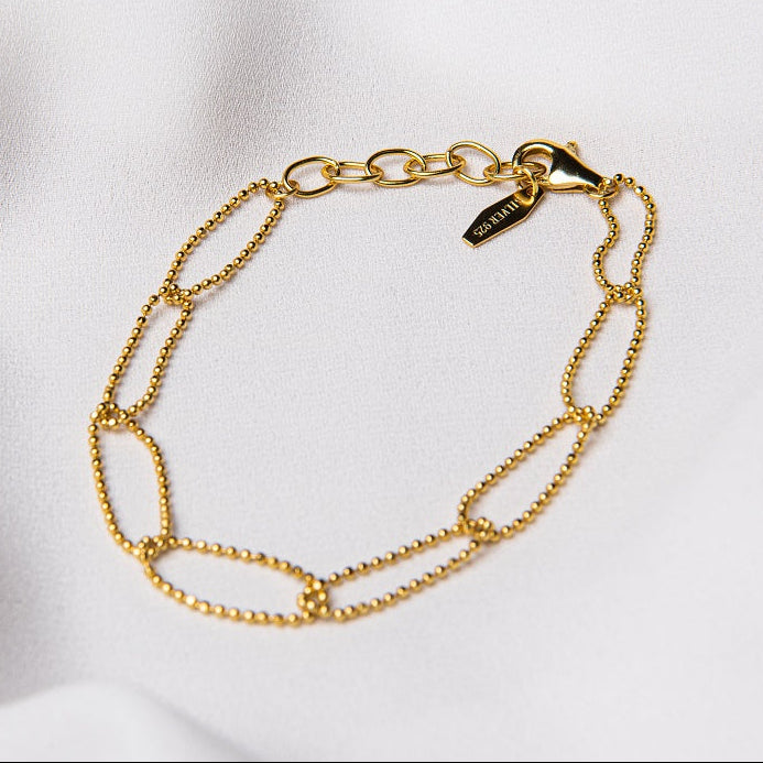 A sterling gold chain bracelet with a clasp, placed on a white fabric surface.