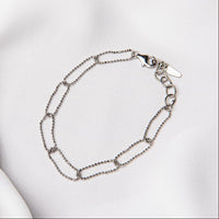 A sterling silver chain bracelet with a clasp, placed on a white fabric surface.
