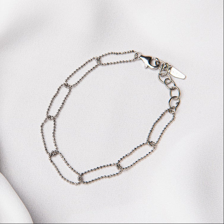 A sterling silver chain bracelet with a clasp, placed on a white fabric surface.