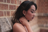 A pair of pearl button stud earrings worn by an asain woman model