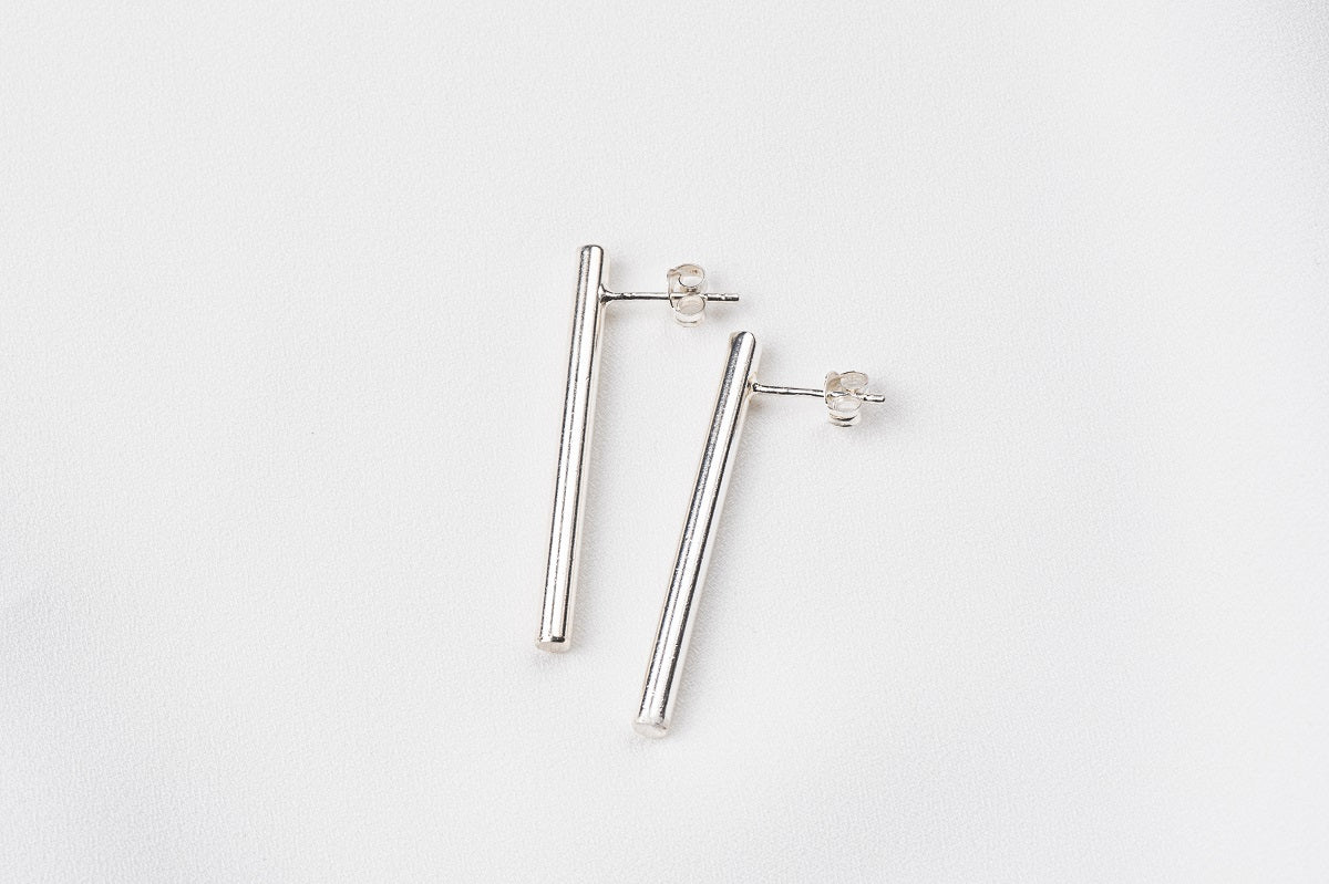 A pair of silver long bar stud earrings on a white background
