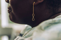A pair of gold-colored dangle earrings with butterfly backs, displayed on a woman model