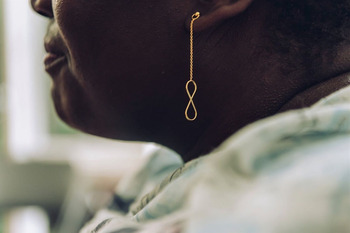 A pair of gold-colored dangle earrings with butterfly backs, displayed on a woman model