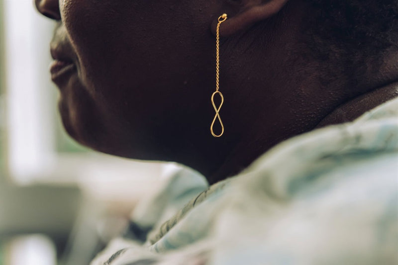 A pair of gold-colored dangle earrings with butterfly backs, displayed on a woman model