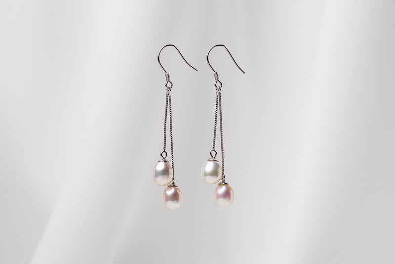 A pair of sterling silver drop earrings with dangling pearls in white, champagne, colors on a white background
