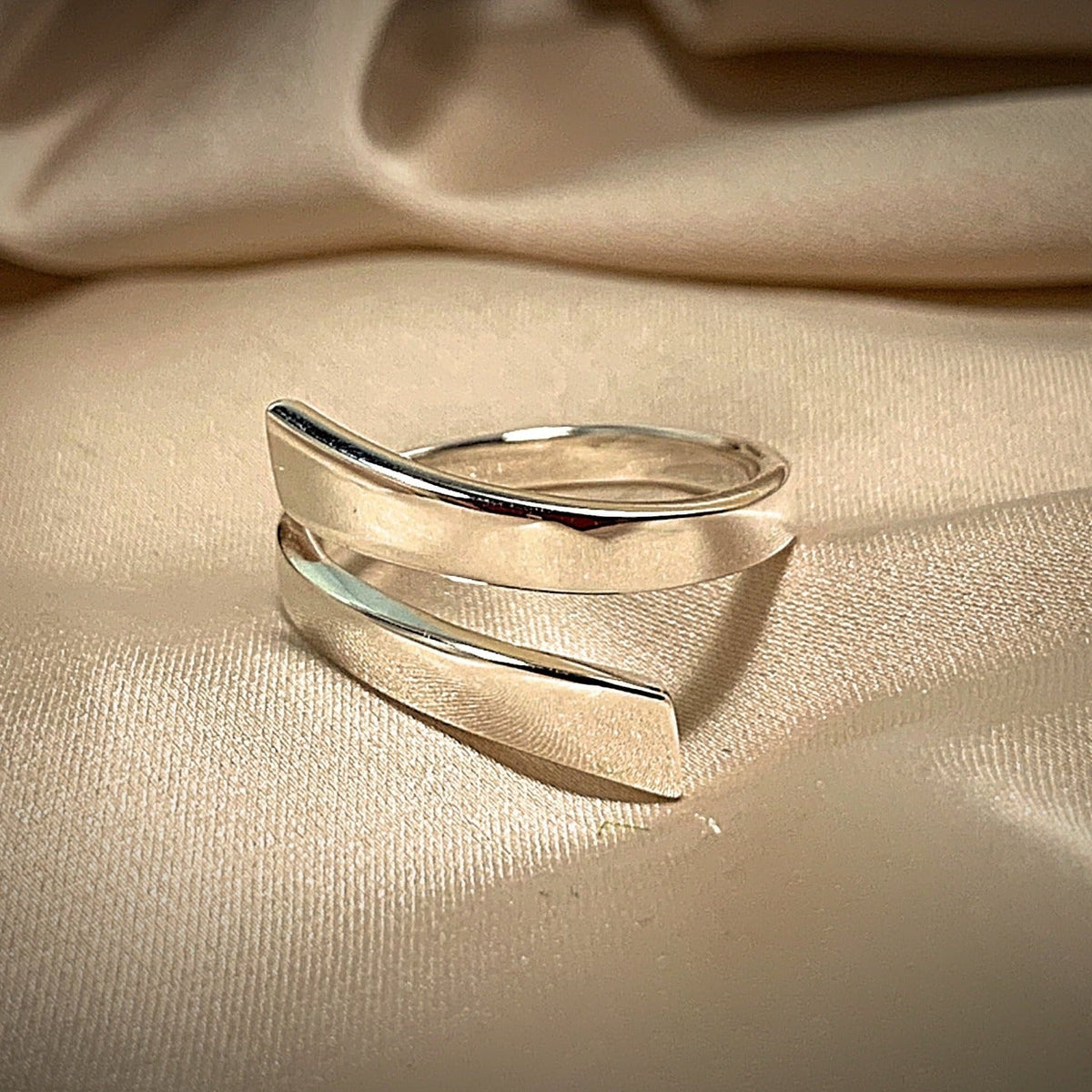 A polished silver ring displayed on a beige fabric surface.