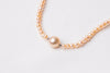 A string of pearls with a larger  champagne pearl in the center displayed on a white background.