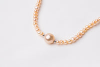 A string of pearls with a larger  champagne pearl in the center displayed on a white background.