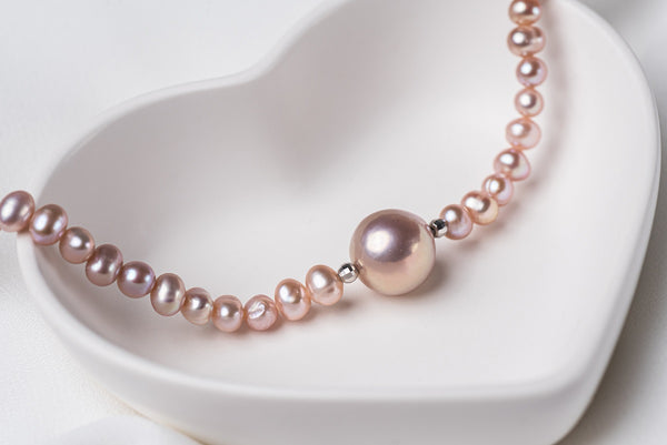 A string of pearls with a larger pearl in the center displayed on a white heart-shaped dish.