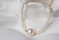 A string of pearls with a larger white pearl with gold vermeil chain in the center displayed on a white background.