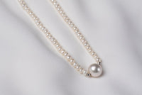 A string of pearls with a larger white pearl in the center displayed on a white background
