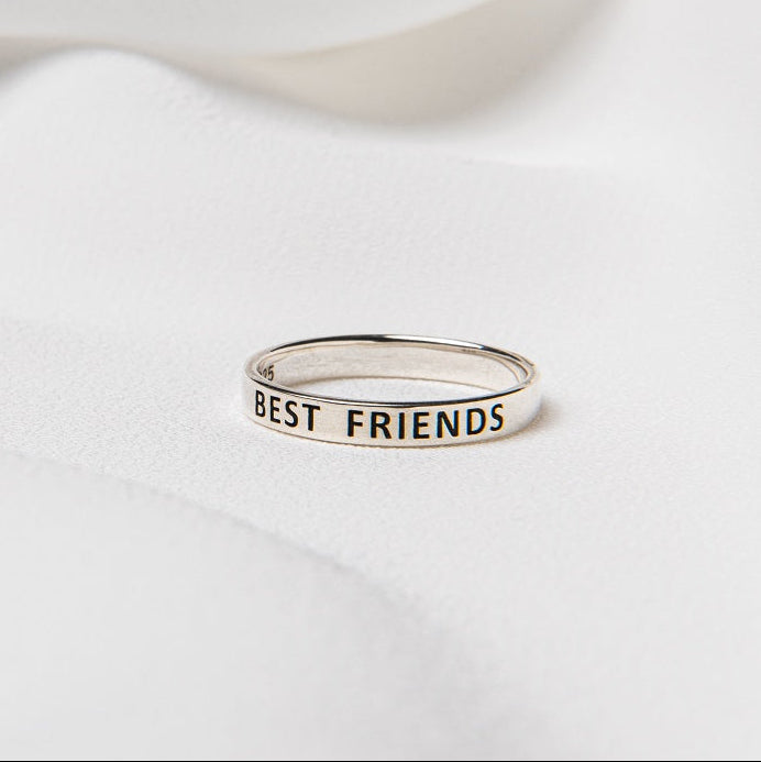 A silver ring with the inscription 'Best Friends' displayed on a white fabric surface.
