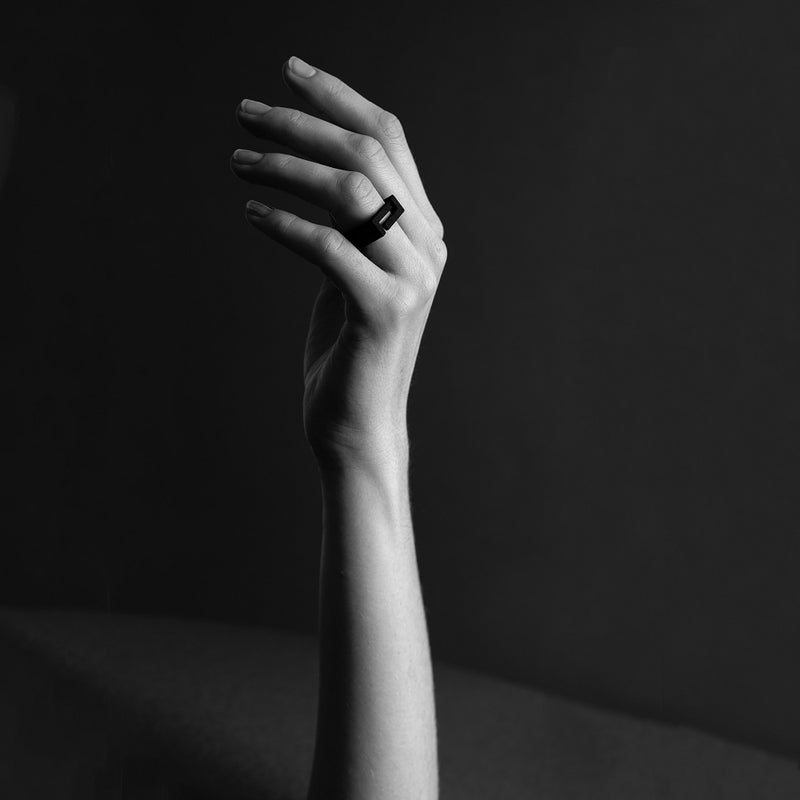 black and white picture of a close up of a hand wearing a matt black ring