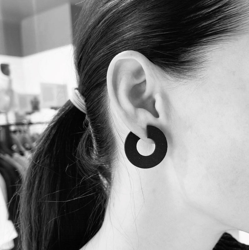 Black and white close up of a woman wearing matt black circular shaped earring.
