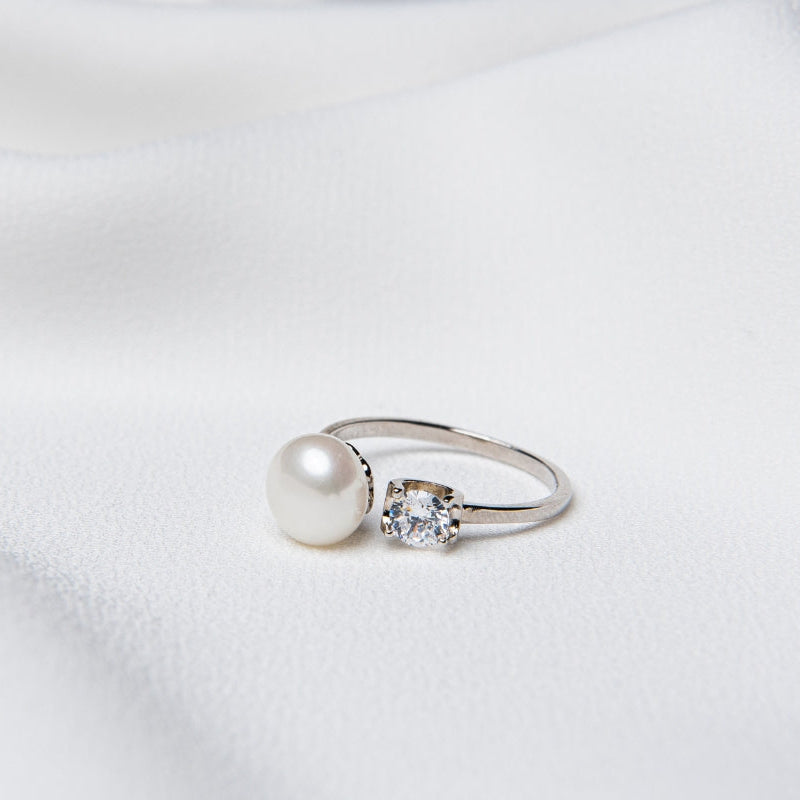 A sterling silver and diamond pearl ring on a white textured surface.