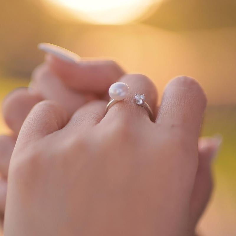 A close up of a womans hand wearing a silver ring featuring a cubic zirconia and a white pearl.