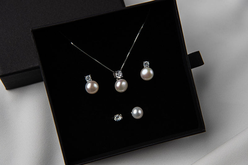 Pearl earrings and matching necklace in a black gift box on a white background
