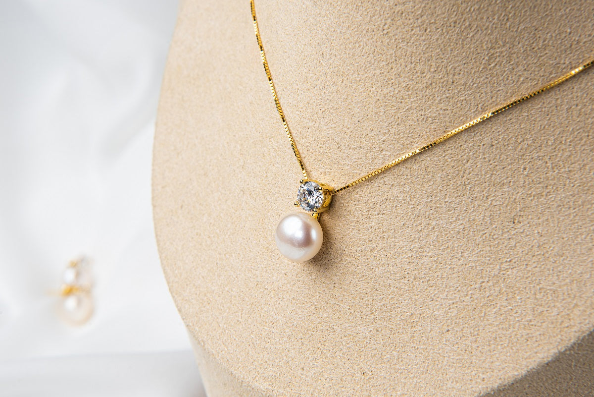 Gold chain necklace with a cubic zirconia and pearl pendant on a bust