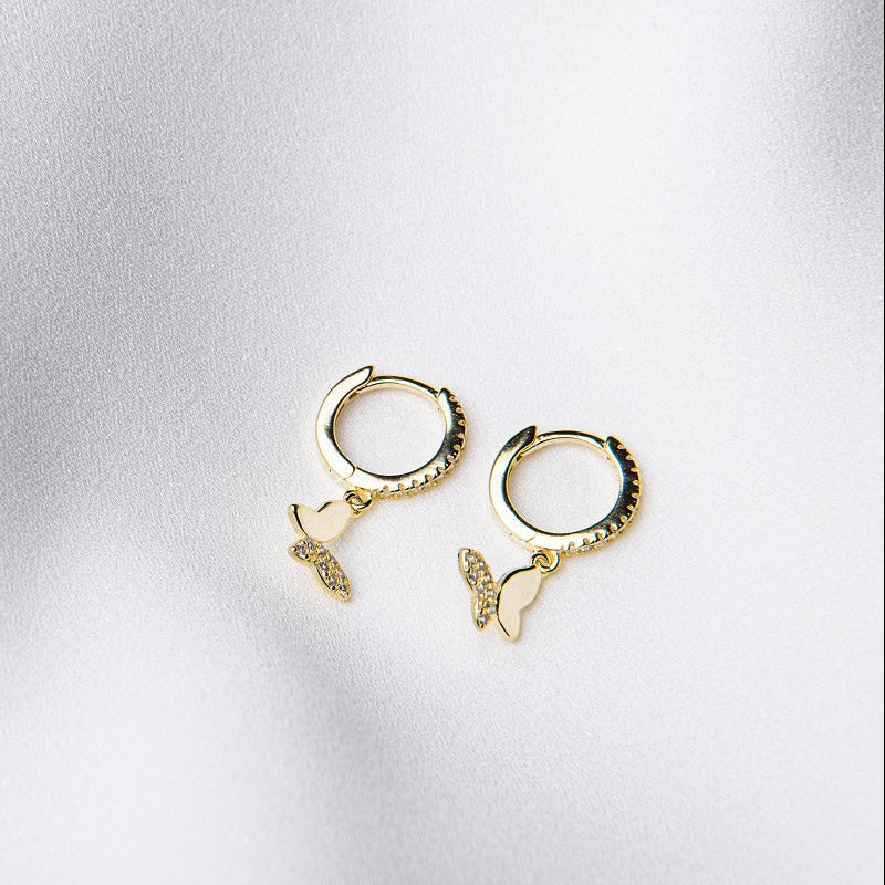A pair of gold vermeil huggie earrings with a butterfly design, placed on a white surface.