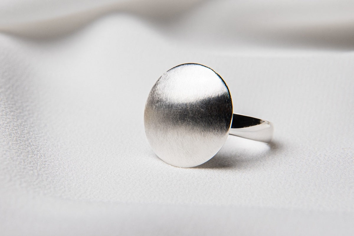 A sterling silver ring with a matte dome top and polished band, displayed on a white fabric surface.