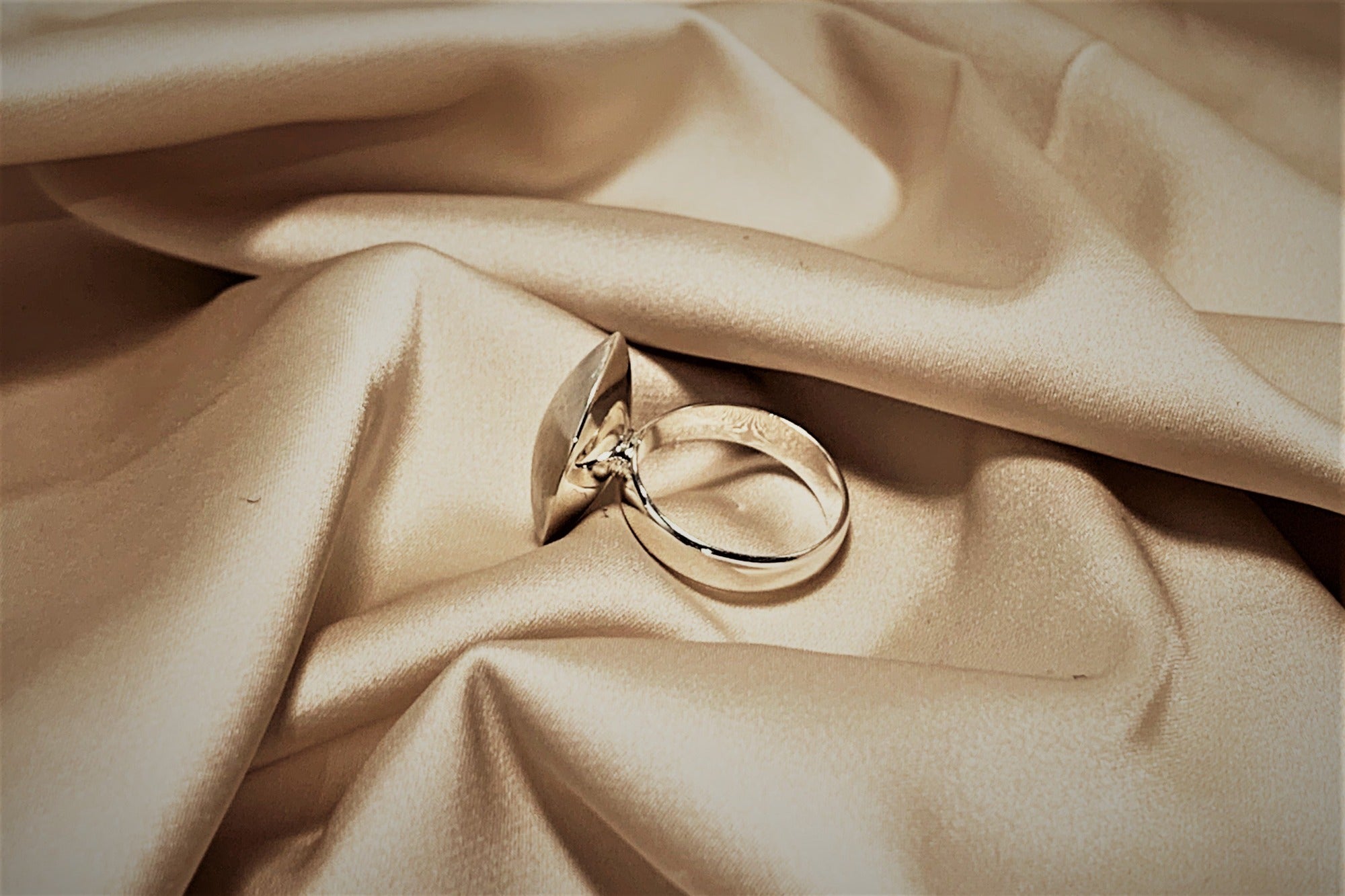A silver ring with a polished band and a textured button shaped top on a cloth background