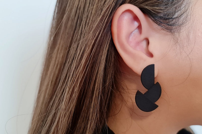 close up of a woman wearing matt black eaerring shaped in 3 overlapping half circles