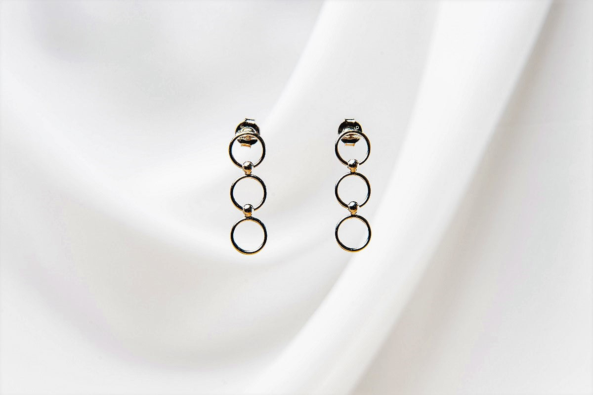 A pair of silver hoop earrings dangle on a white fabric background.