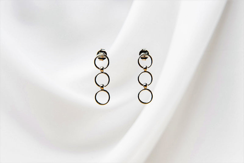 A pair of silver hoop earrings dangle on a white fabric background.